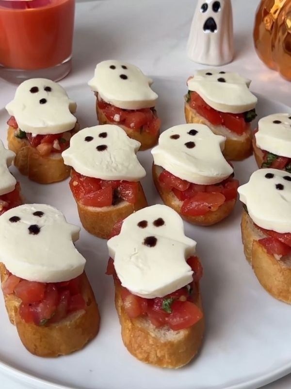 Toasted baguette slices topped with tomato‑basil mix, mozzarella “eyes,” and basil leaf “fangs.”